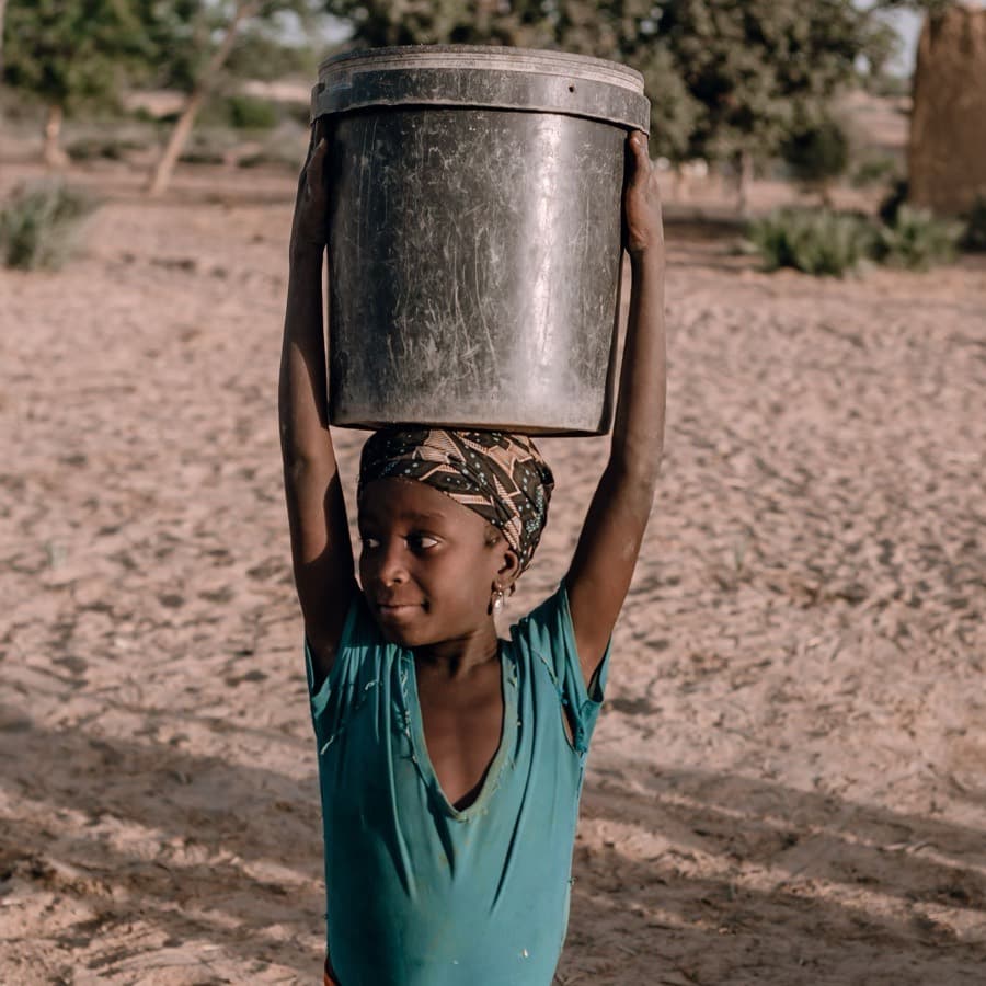 A girl carrying a water bucket balanced on her head in a village